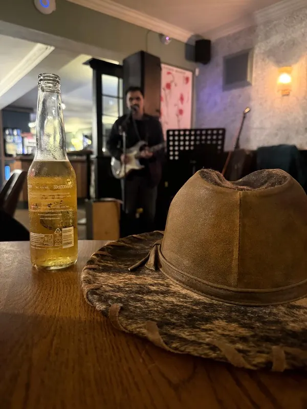 A hat and a bottle of beer on a table at The Oak, with a guitarist singing into the microphone behind